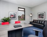 innspace deluxe executive office. Large room with 2 large windows, large desk and black chair with 2 red modular arm chairs. Large black leather sofa and modern wall art.